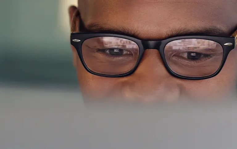 Close-up of a man wearing glasses looking at a computer screen.