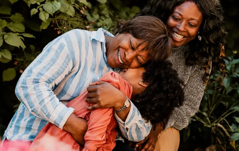Three family members smiling and embracing outdoors.