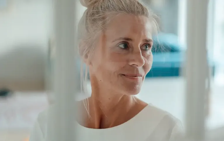 Older woman with light hair tied back, smiling softly while looking to the side.
