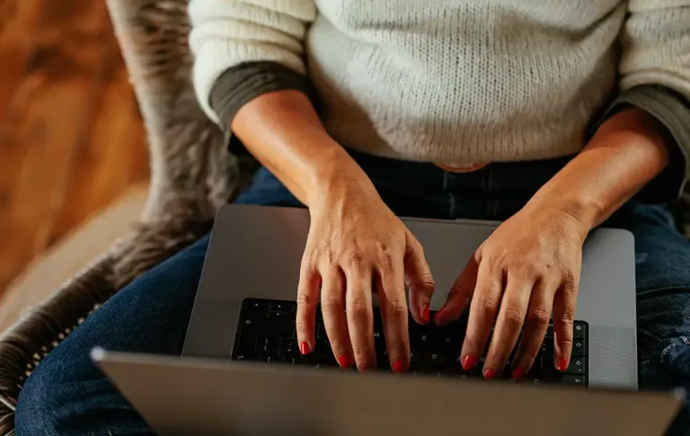 Close-up of a person typing on a laptop while seated.