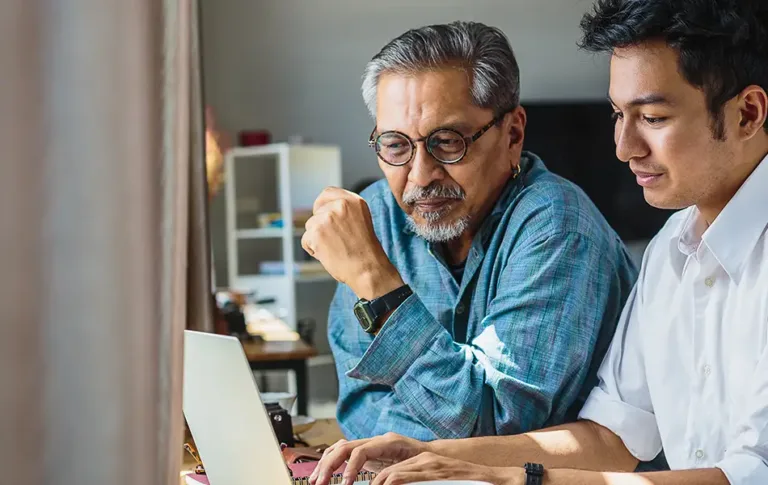 Two men sitting together and looking at a laptop screen.