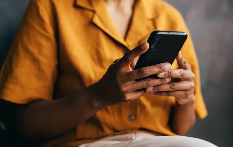 Person wearing a yellow shirt holding a smartphone with both hands.